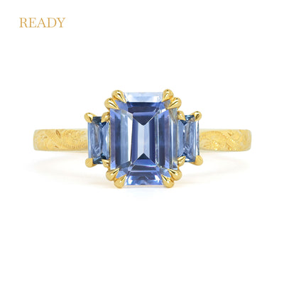 Lebrusan Studio Fancy Athena trilogy engagement ring with hand-engraved 18ct yellow Fairmined Eco Gold band and three emerald cut blue sapphires of ethical traceable origin